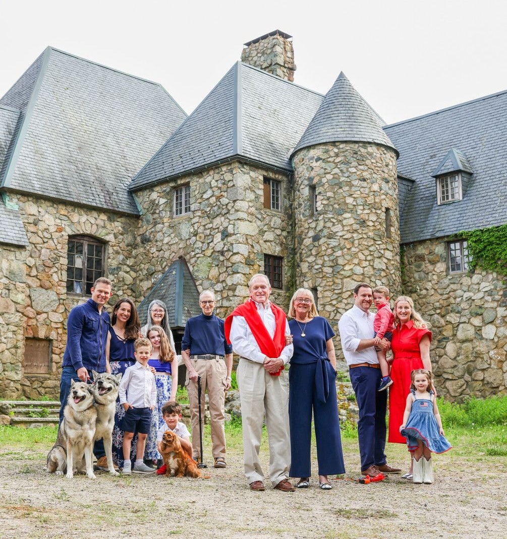 Three generations of the family, with their dogs, standing in front of Hilltop Castle's stone facade and turret